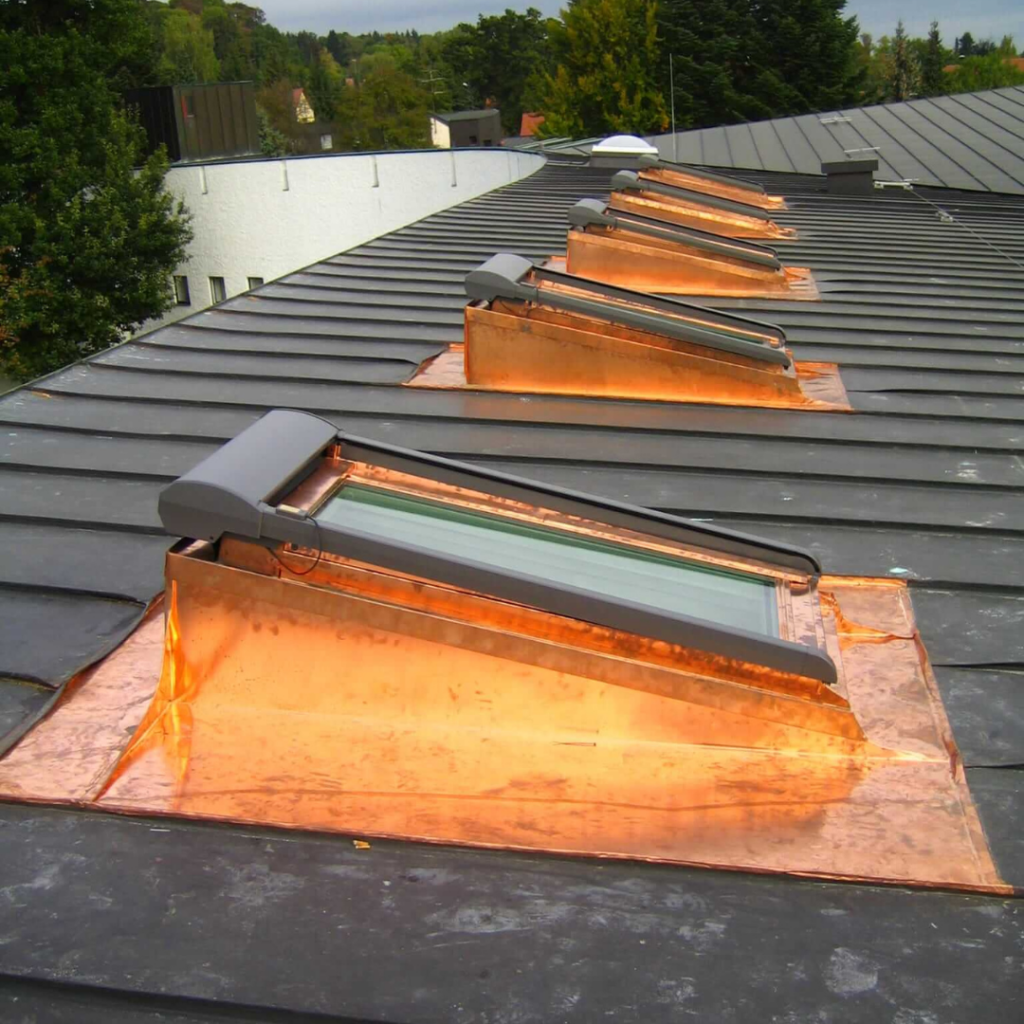 Mehrere moderne Dachfenster mit hochwertigen Kupfereinfassungen auf einem dunklen Stehfalzdach. Langlebige und wetterfeste Dachlösung für optimale Belichtung.