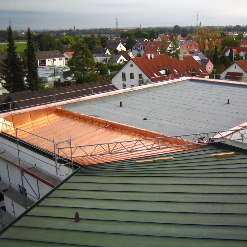 Flachdach eines Gebäudes in der Abdichtungsphase mit umlaufender Kupferverkleidung und moderner Dachentwässerung. Hochwertige Dachabdichtung für optimalen Wetterschutz.