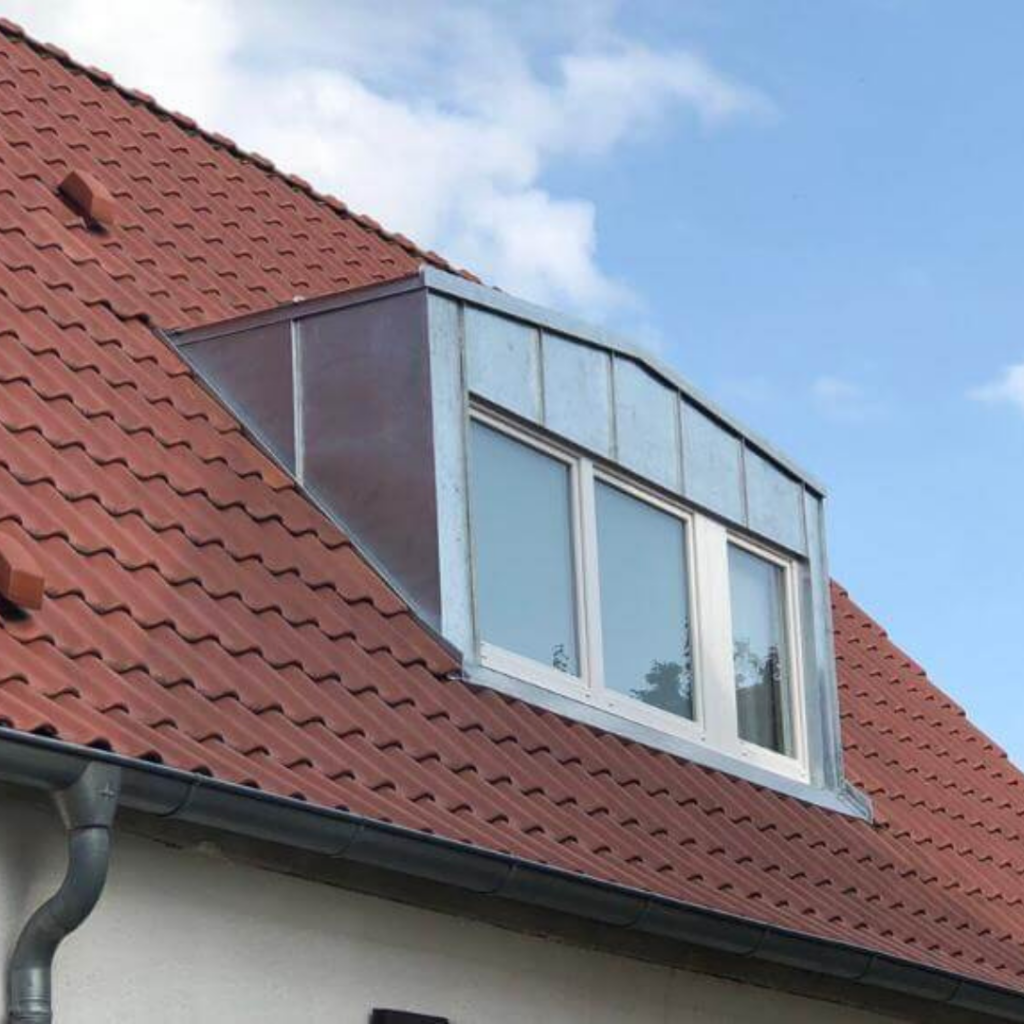 Dachgaube mit verzinkter Metallverkleidung und großen Fenstern auf einem roten Ziegeldach. Wetterbeständige Gaubenlösung für eine langlebige Dachkonstruktion.