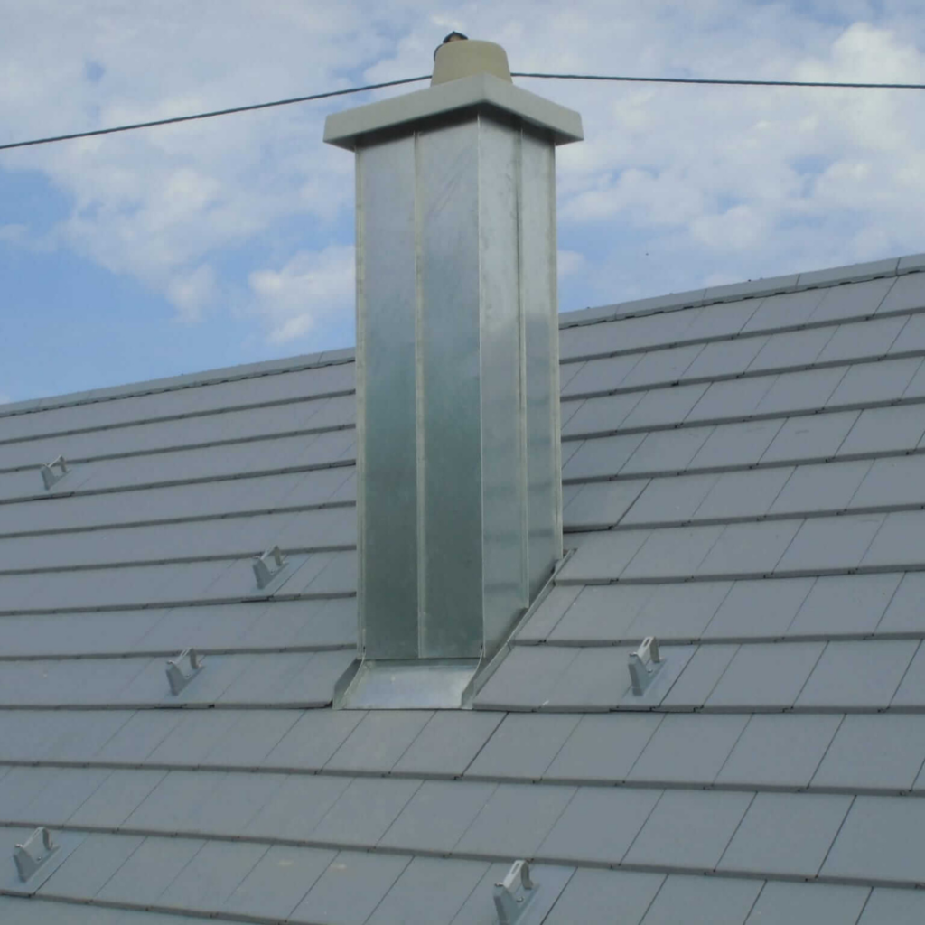 Dach mit grauen Ziegeln und einem verzinkten Schornstein. Die Metallverkleidung schützt den Kamin vor Witterungseinflüssen und sorgt für eine langlebige Dachlösung.