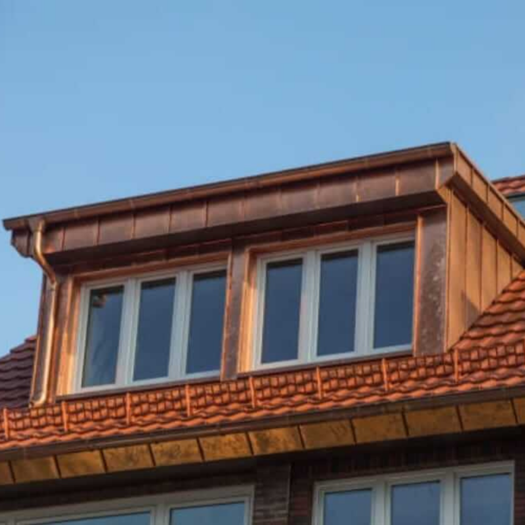 Dachgaube mit edler Kupferverkleidung und großen Fenstern auf einem Ziegeldach. Die Patina-Entwicklung sorgt für eine langlebige und stilvolle Dachgestaltung.
